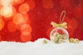 Beautiful transparent Christmas ornament with small golden balls on snow against red background, bokeh effect. Space for text Royalty Free Stock Photo