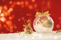 Beautiful transparent Christmas ornaments with golden bows on snow against red background, bokeh effect. Space for text Royalty Free Stock Photo