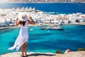 A traveler woman in a white dress enjoys the view to Mykonos, Greece