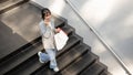 A beautiful Asian woman is talking on the phone while walking down the stairs with her shopping bags Royalty Free Stock Photo