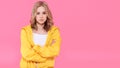 Beautiful trendy girl in bright yellow jacket and crossed arms. Attractive young woman portrait over pastel pink background. Royalty Free Stock Photo