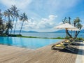 Beautiful tropical swimming pool in hotel or resort with umbrella, coconuts tree sun-loungers, palm trees with infinity pool view Royalty Free Stock Photo