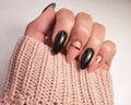 Beautiful two-tone manicure with gold design. Hands in a sweater with black and camouflage gel polish. Royalty Free Stock Photo