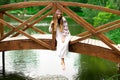 Steep slender Ukrainian woman resting sitting on a wooden decorative bridge over the water on a hot sunny day