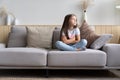 Beautiful unhappy sad little 6-year old girl sitting cross legged on couch in living room Royalty Free Stock Photo