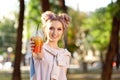 Beautiful urban teenager girl with bun and makeup dressed in a pink T-shirt and a sweatshirt holding a plastic cup with