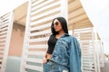 Beautiful urban young hipster woman in a stylish denim jacket in a trendy black top in a vintage jeans skirt in sunglasses resting Royalty Free Stock Photo