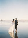 Beautiful vertical back shot of a newly wed couple walking barefoot on the beach Royalty Free Stock Photo