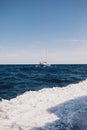 Beautiful vertical shot of the wavy ocean and a ship with the background of blue sky Royalty Free Stock Photo