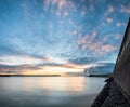 Beautiful vibrant sunrise sky over calm water ocean with lighthouse and harbor wall Royalty Free Stock Photo