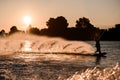 beautiful view of active male rider holds rope and riding on wakeboard on water surface at sunset.