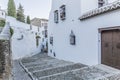 Beautiful view of an alley with houses with white walls, windows with metal lattice, pots with flowers and wooden doors