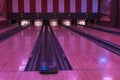Beautiful view of bowling alley interior with pins and five lanes in hall illuminated with purple lighting.
