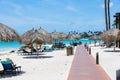 Beautiful view of coast line. Tourists on blue sun beds, white sand and palm trees on blue sky background. Eagle Beach. Royalty Free Stock Photo