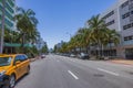 Beautiful view of Collins Avenue in Miami Beach with cars and palm trees on highway against backdrop of blue sky.