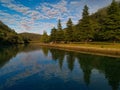 Beautiful view of creek with reflections blue sky, light clouds, fog, mountains and trees on water Royalty Free Stock Photo