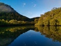 Beautiful view of creek with reflections blue sky, light clouds, fog, mountains and trees on water Royalty Free Stock Photo