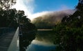 Beautiful view of creek with reflections suspension bridge, blue sky, light clouds, fog, mountains and trees on water Royalty Free Stock Photo