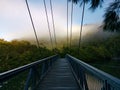 Beautiful view of creek with reflections suspension bridge, blue sky, light clouds, fog, mountains and trees on water Royalty Free Stock Photo