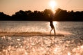 beautiful view of dark silhouette of active male rider holds rope riding on wakeboard on water surface at sunset.