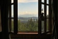 Beautiful view on green forest, blue sky and mountains through a wooden window frame of an old house cottage on a slope of a hill Royalty Free Stock Photo