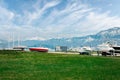 Beautiful view of green lawn in front of embankment with boats on land on trailer against the backdrop of snow-capped mountains.