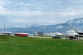 Beautiful view of green lawn in front of the embankment with boats and yacht on land on trailer against the backdrop of snow-c