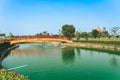 Beautiful view of Japanese style red wooden bridge over emerald pond with fountains against nature of paddy field outdoors. Royalty Free Stock Photo