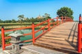 Beautiful view of Japanese style red wooden bridge over emerald pond with fountains against nature of paddy field outdoors. Royalty Free Stock Photo