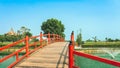 Beautiful view of Japanese style red wooden bridge over emerald pond with fountains against nature of paddy field outdoors. Royalty Free Stock Photo