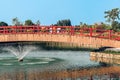 Beautiful view of Japanese style red wooden bridge over emerald pond with fountains against nature of paddy field outdoors. Royalty Free Stock Photo