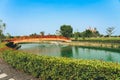 Beautiful view of Japanese style red wooden bridge over emerald pond with fountains against nature of paddy field outdoors. Royalty Free Stock Photo