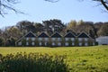 Beautiful view of long house with patterns in roof and windows seen among tree branches and spring daffodils and golf course Royalty Free Stock Photo