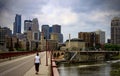A Woman Walks on the Stone Arch Bridge With The Minneapolis, Minnesota Skyline in the Background.