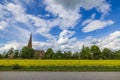 Beautiful view of older church building between green trees behind yellow rapeseed field on blue sky with puffy white clouds. Royalty Free Stock Photo