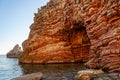 Beautiful view of orange cliff with tunnel standing in sea off the rocky coast. Waves calmly wash rock, rays of sun warm earth.