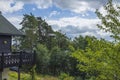 Beautiful view of part facade of typical wooden Swedish house with wooden patio. Tops of green forest trees on blue sky.