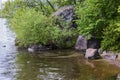 Beautiful view of rocky shoreline of lake with growing shrubs and trees. Royalty Free Stock Photo