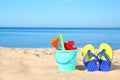 Beautiful view of sand with plastic beach toys and flip flops near sea on sunny day. Space for Royalty Free Stock Photo