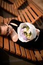 Beautiful view on stylish dressed girl lying on bench and holding delicate mix of fresh flowers in white craft paper Royalty Free Stock Photo