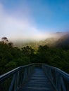 Beautiful view of suspension bridge with blue sky, light clouds, fog, mountains and trees in the background Royalty Free Stock Photo