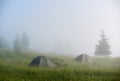 Two camp tents in misty grass field.