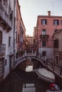 Empty streets and bridges of Venice, A small bridge and pink orange houses reflecting over a canal and a traditional gondola