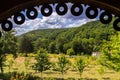 Beautiful view from under the canopy gazebo to the garden with young trees and green mountain slopes against the