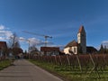 Village Hagnau, Lake Constance with catholic church St. Johann Baptist, road and bare vineyards in front on sunny day in winter. Royalty Free Stock Photo