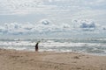 Beautiful view of wavy sea and people standing on the beach on a sunny day with dramatic clouds.