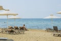 Beautiful view of white sand Greece beach. Sunbeds under sun umbrellas with tourists on turquoise water background. Royalty Free Stock Photo