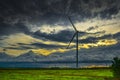 Beautiful view of windmill with green grass on floor and dramatic clouds above during evening hours Royalty Free Stock Photo