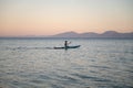 Beautiful view of young boy sitting on sup board paddling on calm evening sea