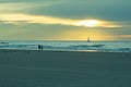 Beautiful warm sunset with sailboat in the background and 2 people walking on the beach along the Belgian coastline Royalty Free Stock Photo